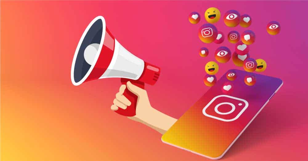 Hand holding a megaphone with social media icons and emojis emerging from a smartphone.